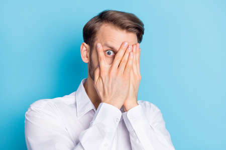 Photo of amazed shocked young man hold hands cover face peek eye hide isolated on pastel blue color...