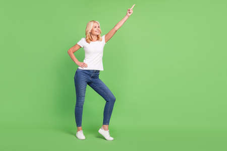 Full size photo of cool blond aged lady point empty space wear white t-shirt jeans isolated on green...