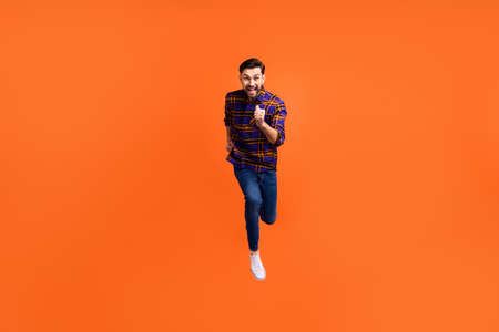 Full size photo of crazy cheerful man jumping running toothy smile isolated on orange color...