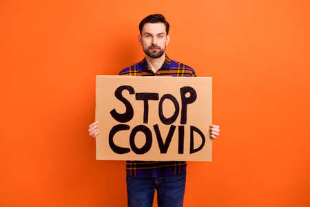 Portrait of young person hands hold paper stop covid placard look camera isolated on orange color backgroundの写真素材