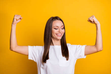Photo portrait of fit woman showing biceps isolated on vivid yellow colored backgroundの写真素材