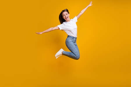 Full length body size photo of careless playful girl jumping keeping hands like wings plane isolated...