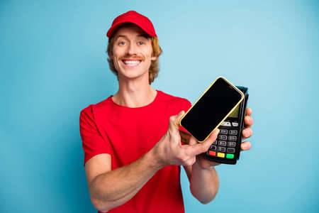 Photo of cheerful handsome guy arms hold phone pos terminal make purchase isolated on blue color...
