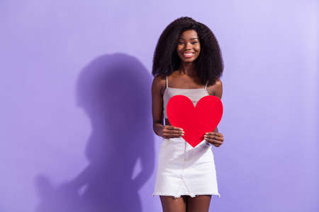 Photo of young cheerful afro woman happy positive smile hold big red paper heart love romantic isolated over violet color backgroundの写真素材