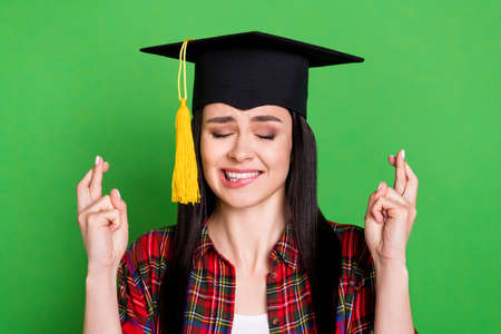Photo of brunette beg young lady crossed fingers wearing graduate cap red shirt isolated on green color backgroundの写真素材