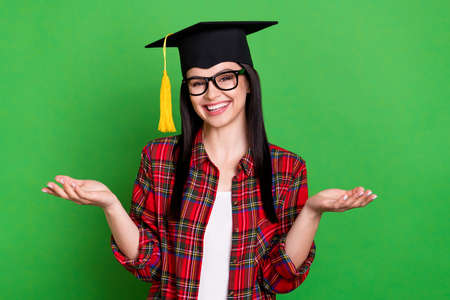 Photo of brunette clueless young lady shrug shoulders wearing graduation cap spectacles red shirt isolated on green color backgroundの写真素材