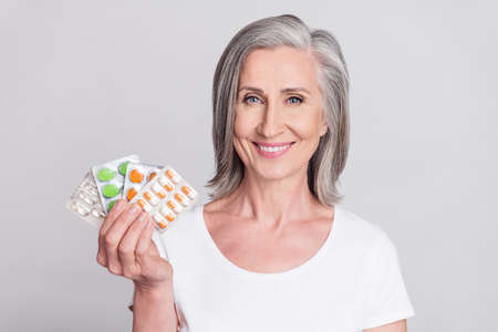 Photo of elderly woman happy positive smile show meds painkillers vitamins health isolated over grey color backgroundの写真素材