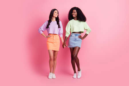 Full size photo of cute ladies wear cropped sweater mini skirt hold hands isolated on pastel pink color backgroundの写真素材