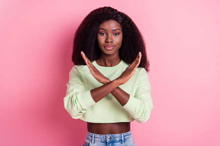 Photo of serious young dark skin woman make hands cross prohibition isolated on pastel pink color backgroundの写真素材