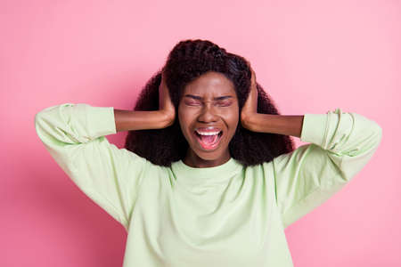 Photo of unhappy sad dark skin young woman hold hands head cover ears isolated on pastel pink color backgroundの写真素材