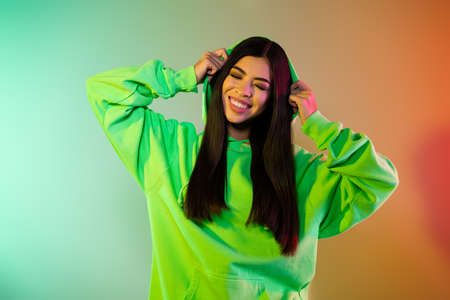 Portrait of attractive dreamy cheerful girl resting clubbing free time isolated over multicolor vivid neon light backgroundの写真素材