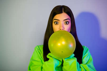 Photo of stunning funny young woman dressed green hoodie blowing balloon empty space isolated neon...