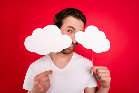 Photo of curious young brown hairdo man cover face by clouds wear white t-shirt isolated on red color backgroundの写真素材