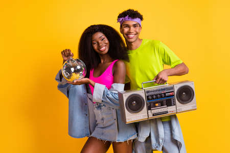 Photo of sweet charming young people wear jeans clothes holding disco ball boombox dancing isolated yellow color backgroundの写真素材