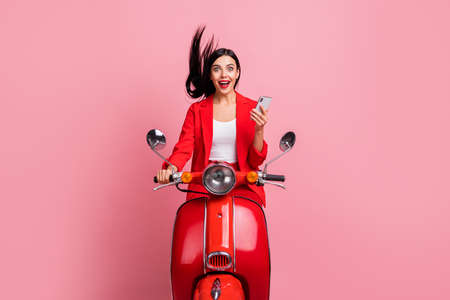 Photo of young excited girl happy positive smile amazed surprised browse cellphone ride bike isolated over pink color backgroundの写真素材