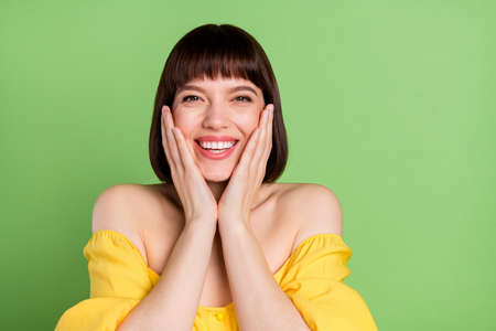 Photo of adorable happy attractive young woman hold hands face cheeks isolated on green color backgroundの写真素材