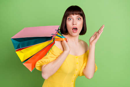 Portrait of attractive amazed girl carrying new things clothes bags wow bargain isolated over green color backgroundの写真素材