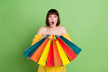 Photo of amazed excited young woman hold hands bags sale shock purchase isolated on green color backgroundの写真素材