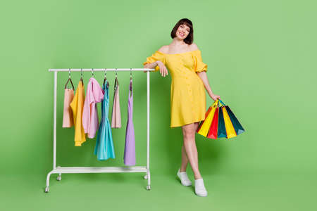 Full length photo of cheerful happy young woman hold bag smile shopping center rack isolated on green color backgroundの写真素材
