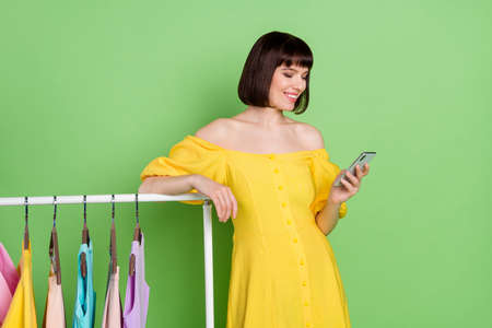 Photo of cheerful young nice brunette bob haired woman wear yellow dress look phone showroom isolated on green color backgroundの写真素材