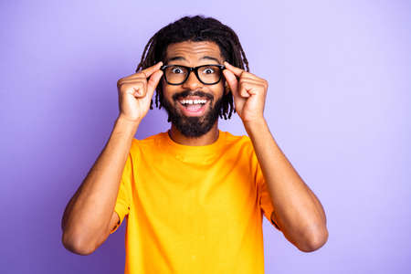 Portrait of nice optimistic brunet guy touch spectacles wear orange t-shirt isolated on vibrant lilac color backgroundの写真素材