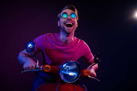 Portrait of attractive amazed cheerful guy riding bike having fun isolated over dark neon purple...