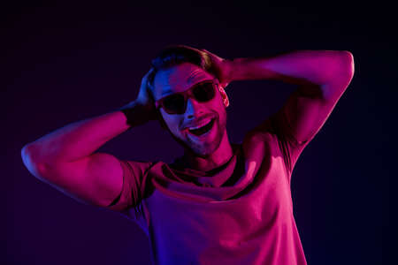 Portrait of attractive cheerful funny guy touching hair having fun isolated over dark neon violet color backgroundの写真素材