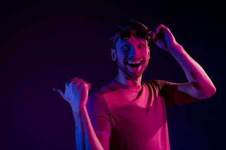 Portrait of attractive amazed cheerful guy demonstrating copy space offer advert isolated over dark neon violet color backgroundの写真素材