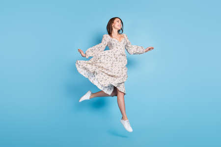 Full body photo of nice brown hairdo young lady jump look empty space wear dress isolated on blue backgroundの写真素材