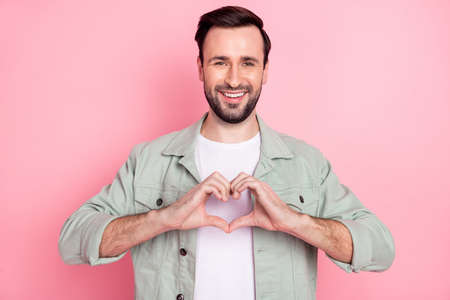 Portrait of attractive cheerful glad guy showing heart shape feeling amour isolated over pink pastel color backgroundの写真素材
