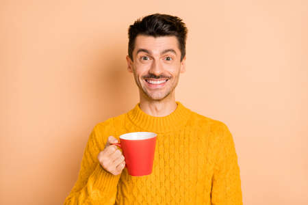 Photo portrait of cheerful smiling man drinking coffee keeping cup isolated on pastel beige color backgroundの写真素材