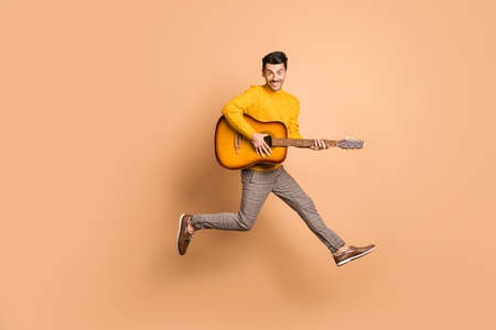 Full length photo portrait of guy playing guitar jumping up isolated on pastel beige colored...
