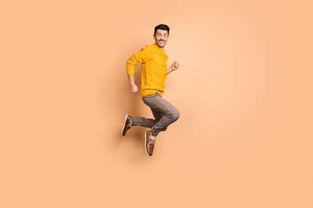 Full length photo portrait side profile of excited man jumping up isolated on pastel beige colored...