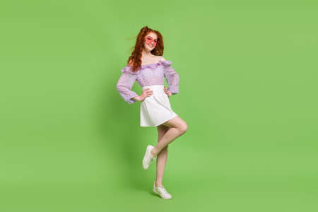 Full size photo of optimistic red hairstyle young lady stand wear blouse skirt spectacles isolated on green color backgroundの写真素材