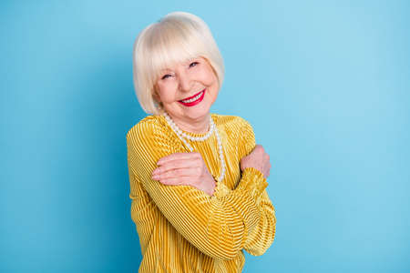 Photo of cheerful short hairdo mature lady hug herself wear blouse necklace isolated on blue color...
