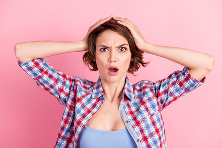 Photo portrait of shocked panicking woman holding head with two hands open mouth isolated on pastel pink colored backgroundの写真素材