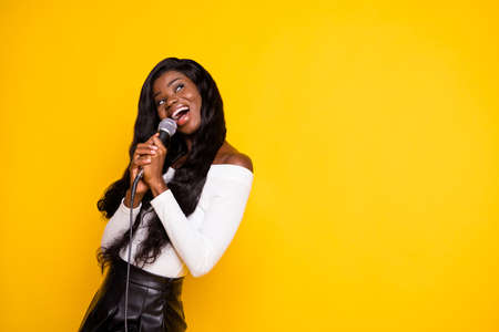 Photo portrait of curious black skinned woman singing song keeping microphone looking copyspace isolated vibrant yellow color backgroundの写真素材
