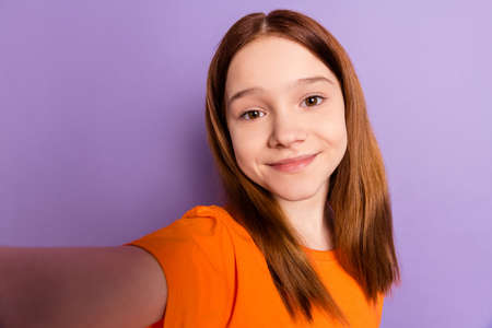 Photo of optimistic nice ginger hair girl do selfie wear orange t-shirt isolated on purple color backgroundの写真素材