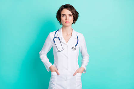 Photo of young woman serious confident doctor therapist hands in pocket isolated over teal color backgroundの写真素材