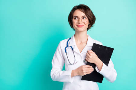 Photo portrait of nurse smiling hugging clipboard wearing white uniform looking copyspace isolated vibrant teal color backgroundの写真素材