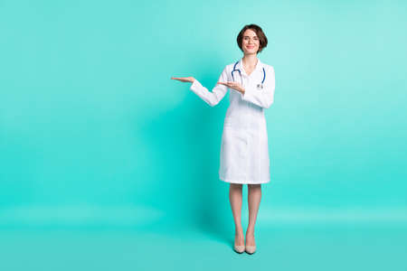 Full length body size photo of nurse smiling showing copyspace on hand isolated bright turquoise color backgroundの写真素材