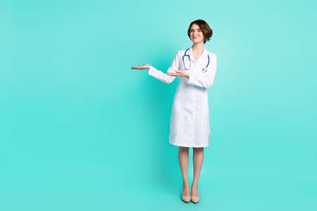 Full length body size photo of nurse smiling showing blank space on hand in glasses isolated vivid turquoise color backgroundの写真素材