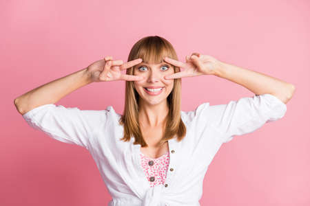 Photo of charming young girl demonstrate two v-signs cover eye wear white blouse isolated pink color...