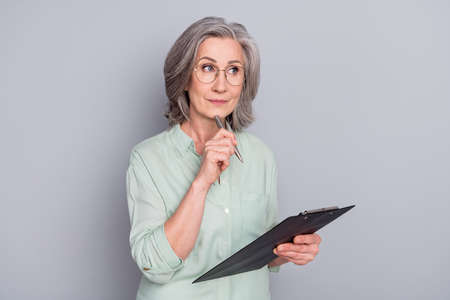 Portrait of attractive minded gray-haired woman creating writing to-do list isolated over grey pastel color backgroundの写真素材