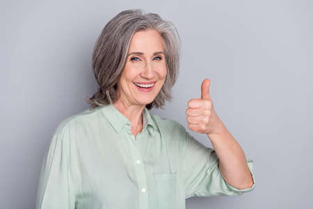 Photo of happy smiling good looking pretty granny showing thumb-up like approval isolated on grey color backgroundの写真素材