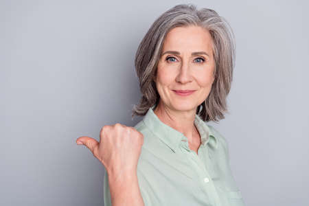 Portrait of attractive cheery gray-haired woman demonstrating copy space ad look idea isolated over gray pastel color backgroundの写真素材