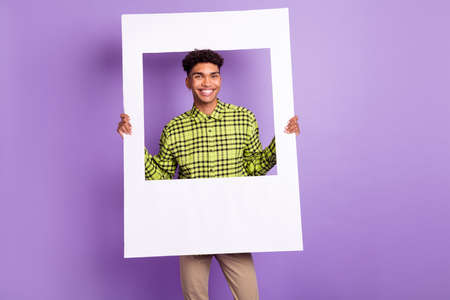 Portrait of attractive funny cheerful brunet guy holding in hands paper frame isolated over violet purple color backgroundの写真素材