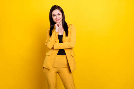 Photo of young attractive woman happy positive smile hand touch chin think wear suit isolated over yellow color backgroundの写真素材