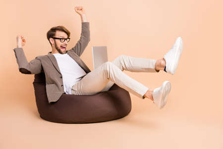 Full size photo of happy excited crazy businessman in glasses raise fists in victory use laptop isolated on beige color backgroundの写真素材