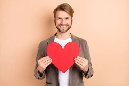 Photo of classy attractive young gentleman dressed blazer holding big red heart empty space isolated beige color backgroundの写真素材